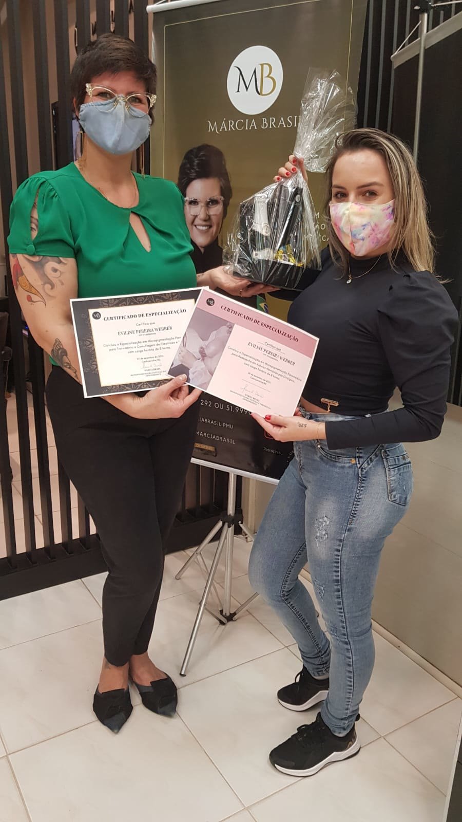 Márcia Brasil entregando certificados a uma aluna, as duas de máscara